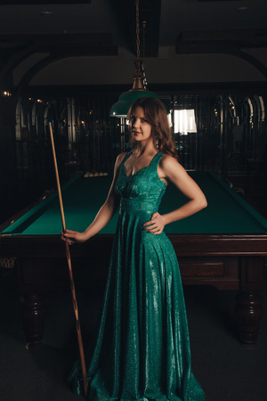 Young woman playing billiards in the dark billiard club.