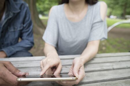Man and Women who use the smart phone in the parkの写真素材