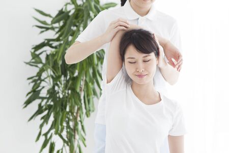 A woman sitting in bed and receiving shoulder and neck massage.の写真素材
