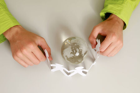 Male hands holding paper people around a glass globeの写真素材