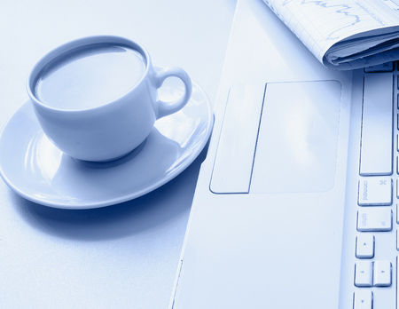 A cup of coffee, paper and a pen on a laptopの写真素材