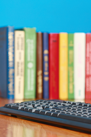Focus on a keyboard lying on a desk with books, over blueの写真素材