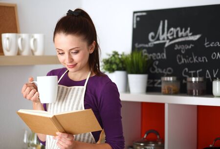 Young woman reading cookbook in the kitchen, looking for recipe .の写真素材