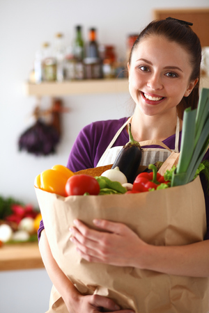 Young woman holding grocery shopping bag with vegetables Standing in the kitchen.の写真素材
