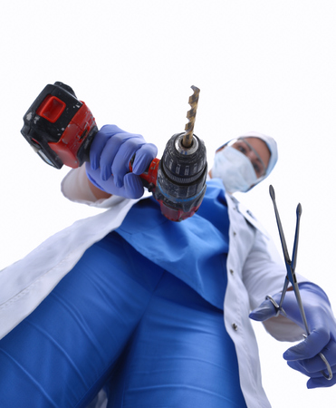 View from below of masked doctor scaring the patient with a drillの写真素材