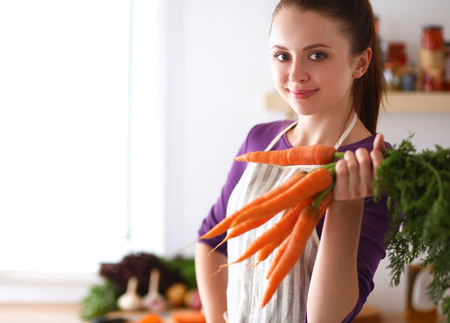 Happy young woman holding bunch of carrots in kitchen.の写真素材