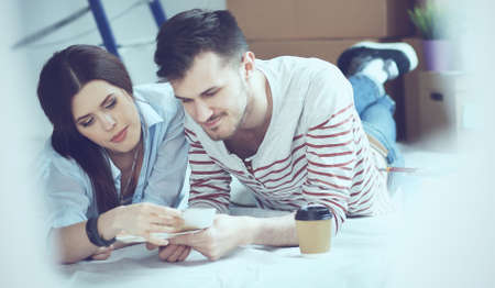 Couple choosing paint colour from swatch for new home lying on wooden floor.の写真素材