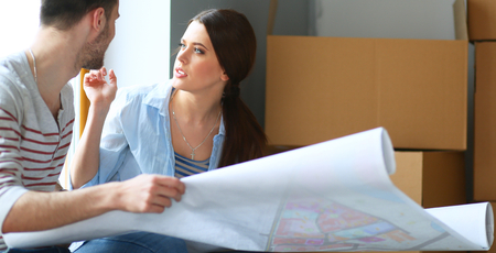 Young couple sitting on the floor and looking at the blueprint of new home.