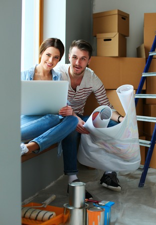 Young couple sitting on the floor and looking at the blueprint of new homeの写真素材
