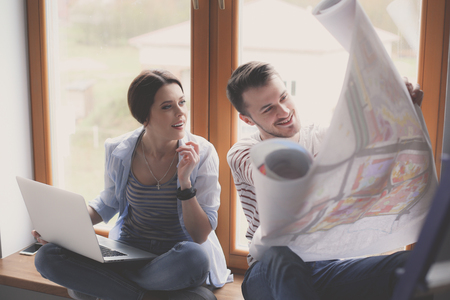 Young couple sitting on the floor and looking at the blueprint of new homeの写真素材