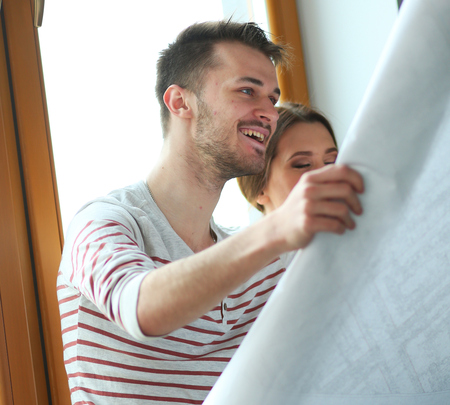 Young couple sitting on the floor and looking at the blueprint of new homeの写真素材