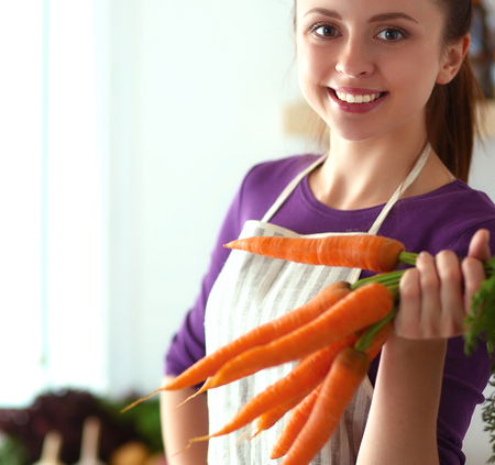 Happy young woman holding bunch of carrots in kitchenの写真素材