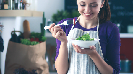 Young woman eating fresh salad in modern kitchenの写真素材