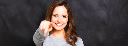 Portrait of a beautiful young woman pointing at you, isolated on gray backgroundの写真素材