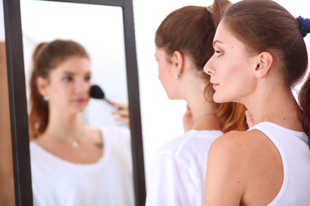 Beautiful girls looking in the mirror and applying cosmetic with a big brushの写真素材