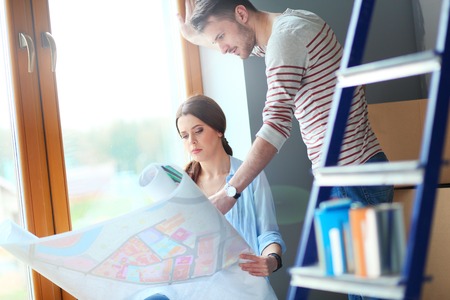 Young couple sitting on the floor and looking at the blueprint of new home
