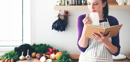 Young woman reading cookbook in the kitchen, looking for recipeの写真素材