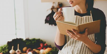 Young woman reading cookbook in the kitchen, looking for recipe .の写真素材