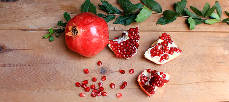 Ripe pomegranate fruit with a branch and leaves on a wooden tableの写真素材