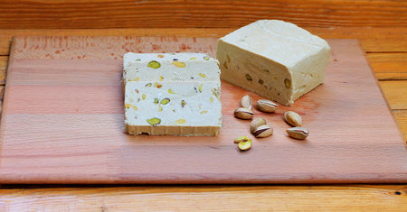 Halva with pistachios on a wooden cutting board on a wooden backgroundの写真素材