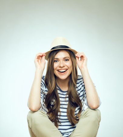 Beautiful young woman sitting relaxed wearing modern hat. Isolated studio portrait.の写真素材
