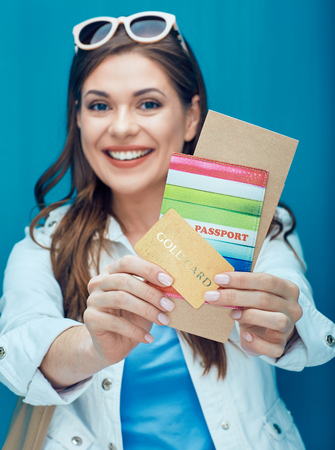 Happy woman showing passport, credit card and ticket for holidays. Blue background.の写真素材