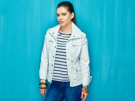 Girl in teen style with long hair standing against blue wall back. Studio fashion portrait.の写真素材
