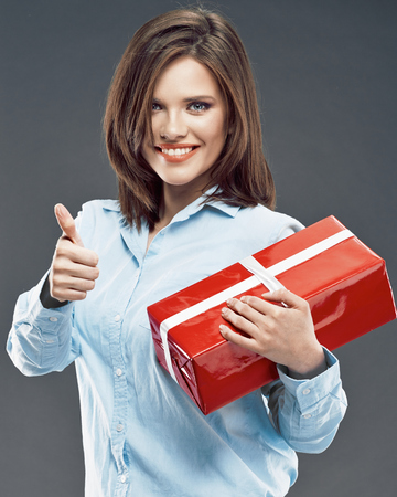 Smiling business woman hold red gift box show thumb up. Studio isolated.の写真素材