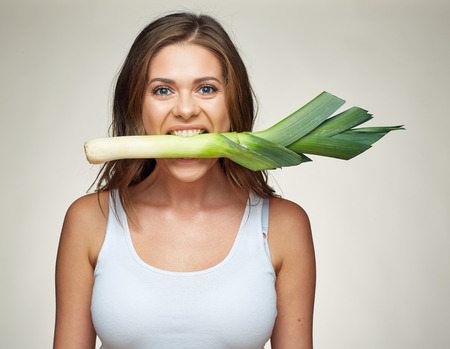 Woman bite green leek. Funny face studio portrait.の写真素材