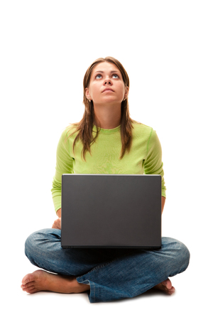 Yong woman sitting on  floop with laptop and looks upwards, isolated over whiteの写真素材