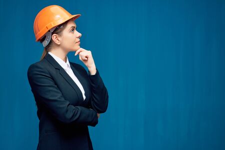 Portrait of thinking business woman wearing builder helmet on blue.