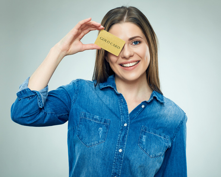 Smiling young woman holding gold credit card against her eye.  Isolated portrait of happy girl.の写真素材