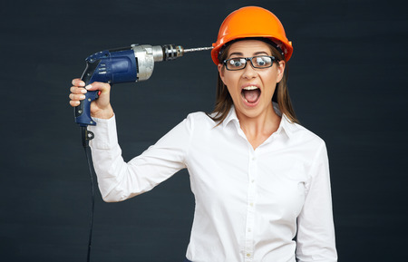Funny portrait of business woman builder drills his head. Black isolated.
