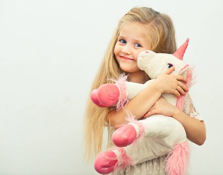 little smiling girl with white unicorn toy. isolated portrait of girl with long blond hair.の写真素材