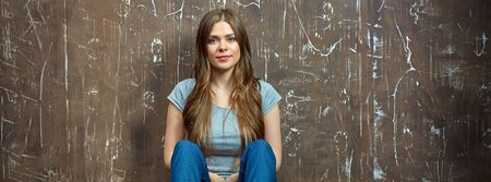 Casual dressed woman with long hair  sitting on a floor. Grunge background wall.