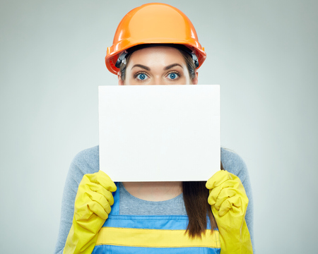 Woman builder holding white banner in front of face. Isolated portrait with safety helmet.の写真素材