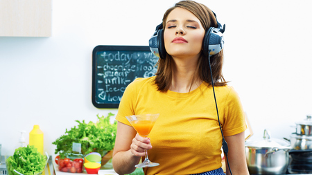 Woman cooking with fun. Girl drinking juice in kitchen and listen music.の写真素材