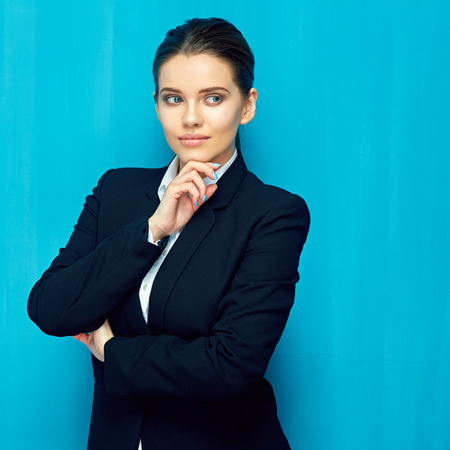 Portrait of thinking businesswoman wearing black suit touching face. blue wal background.の写真素材