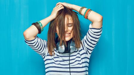 Happy girl with long tail hair style standing with closed eyes against blue wall.の写真素材