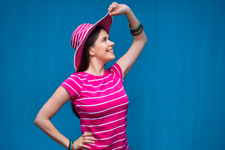 Smiling woman wearing big pink hat looking side. Profile portrait on blue.の写真素材