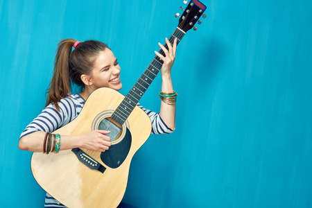 Teen girl play with fun on guitar. Teenager life style concept on blue background .