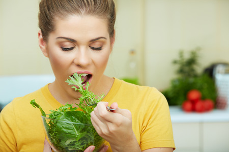 Happy Woman eating vegetarian food, standing against  home kitchen interior background.の写真素材