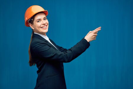 Smiling woman wearing building helmet pointing finger at copy space. Blue background.の写真素材
