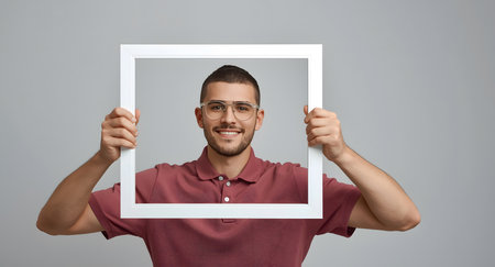 Smiling Man Holding an Empty White Frame Around His Faceの素材