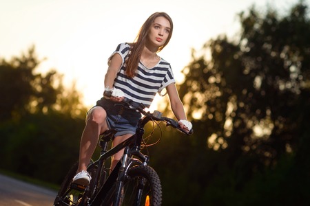 a young girl rides a Bicycle on the road outside the city in the sunset timeの写真素材