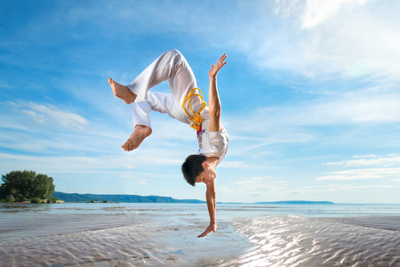 A young guy trains capoeira on the beach - concept about people, lifestyle and sport.の写真素材