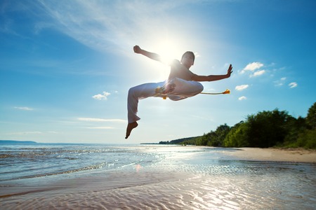 A young guy trains capoeira on the beach - concept about people, lifestyle and sport.の写真素材