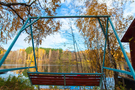 The swing is located in the forest on the lake shore. There is a magnificent view of the autumn blue lake with yellow trees.の写真素材