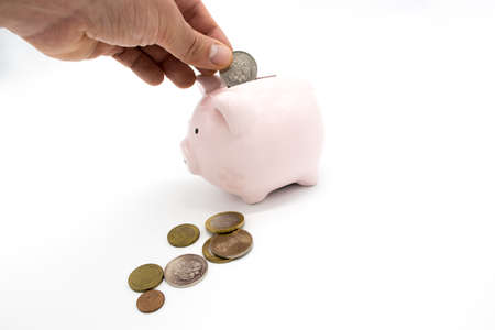 Hand puts banknote in piggy bank in the shape of a pig isolated on white