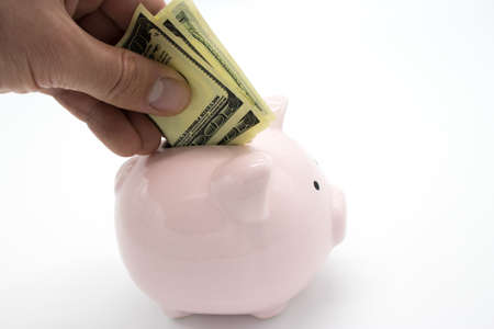 Hand puts banknote in piggy bank in the shape of a pig isolated on white
